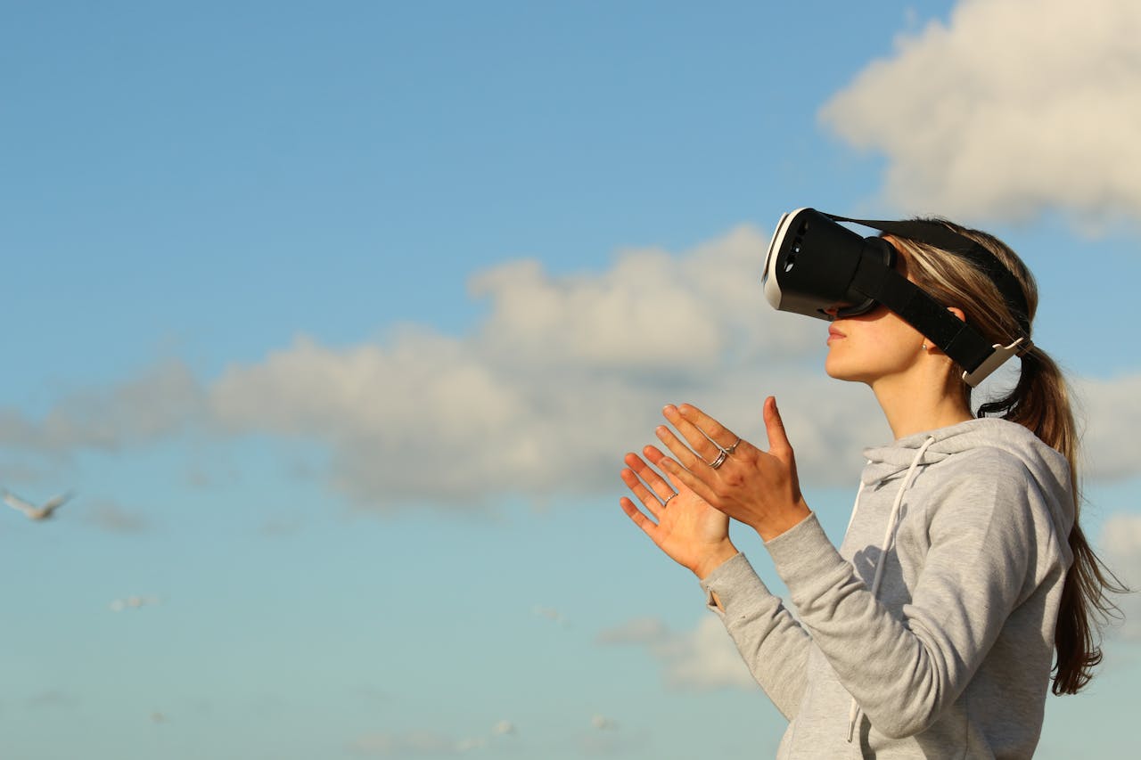 about-us Woman using VR headset outdoors, exploring virtual reality under a clear blue sky.